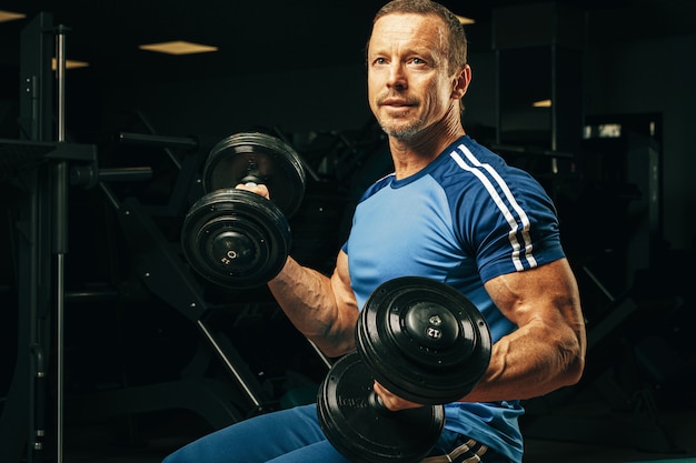 Ajuste senior hombre haciendo ejercicios con pesas en un gimnasio