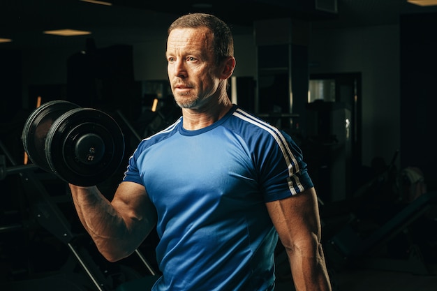 Ajuste senior hombre haciendo ejercicios con pesas en un gimnasio