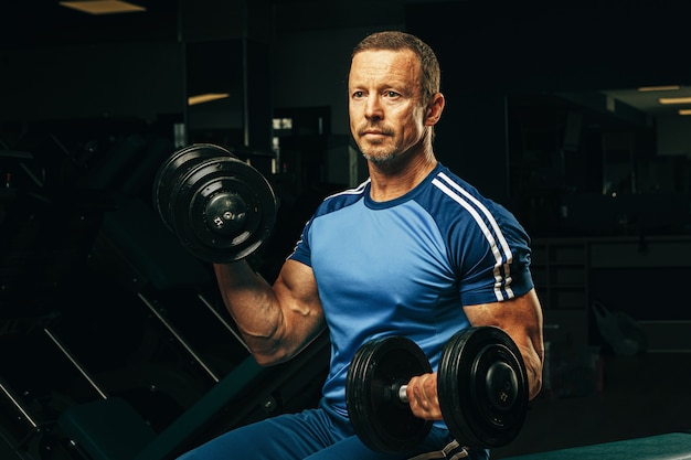 Ajuste senior hombre haciendo ejercicios con pesas en un gimnasio