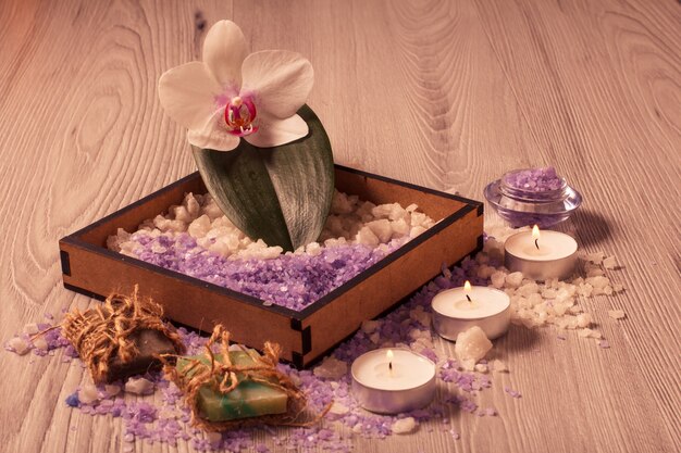 Ajuste de spa con flor de orquídea, caja con sal marina, jabón aromático y velas sobre tabla de madera