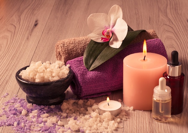 Ajuste de spa con flor de orquídea, cuenco con sal marina, botellas con aceite aromático, velas y toallas sobre tabla de madera