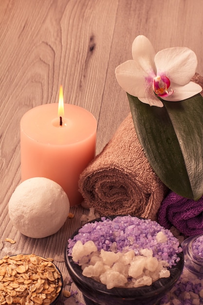 Ajuste de spa con flor de orquídea, cuenco con sal marina, exfoliante, velas y toallas sobre tabla de madera