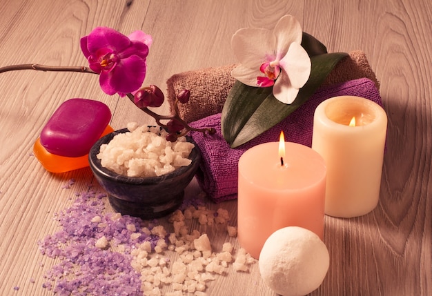 Ajuste de spa con flores de orquídeas, cuenco con sal marina, velas, jabón y toallas sobre tabla de madera