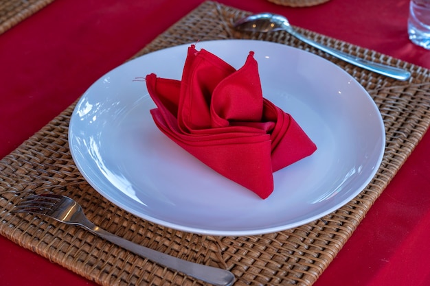 Foto ajuste de la tabla elegante con tenedor, cuchara, plato blanco y servilleta roja en el restaurante, de cerca. bonito juego de mesa de comedor con cubiertos y servilletas