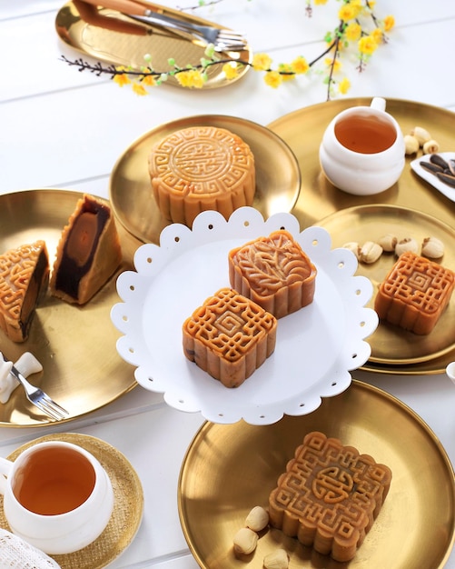 Ajuste de la tabla de Mooncake Mooncake. Pastelería tradicional china de forma cuadrada con tazas de té en la mesa de ratán blanco. Concepto de Festival del Medio Otoño con tema blanco y dorado, de cerca.