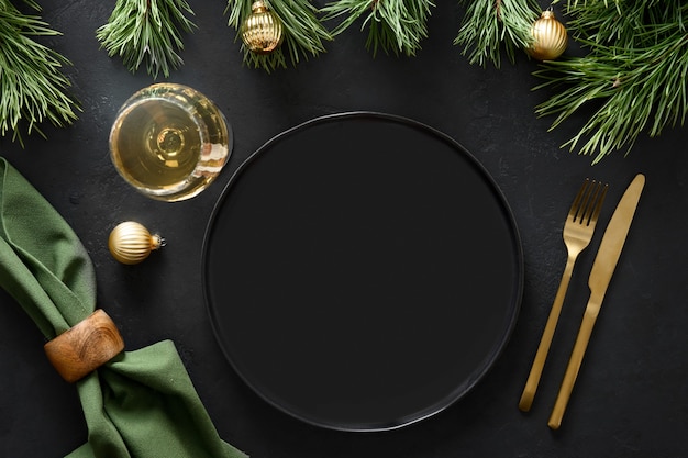 Foto ajuste de la tabla de navidad con decoración dorada, cubiertos y adornos dorados sobre fondo negro.
