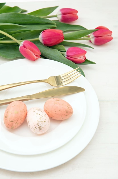 Ajuste de la tabla de Pascua flores de primavera y huevos cubiertos de oro sobre placas de fondo blanco.