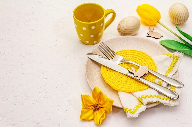 Ajuste de la tabla de Pascua en fondo blanco texturizado de la masilla. Plantilla de tarjeta de vacaciones de primavera. Cubiertos, servilleta tejida, huevo, conejito, tulipán, taza de lunares