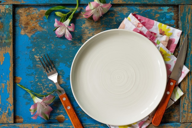 Ajuste de la tabla de primavera o día de la madre, cubiertos de placa y servilleta en la mesa de madera azul