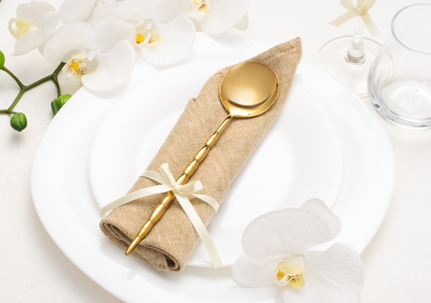 Ajuste de la tabla romántica festiva con servilleta beige y orquídeas blancas sobre un mantel blanco