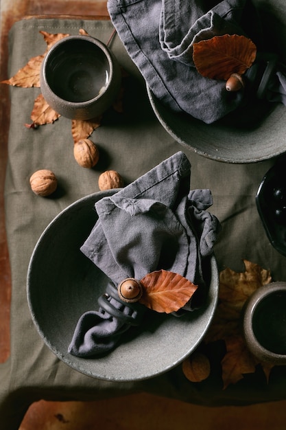 Ajuste de la tabla rústica de Halloween o Acción de Gracias de otoño con vajilla de cerámica artesanal vacía, cuencos grises y tazas sobre un mantel de lino con hojas amarillas de otoño y bellotas y nueces. Endecha plana