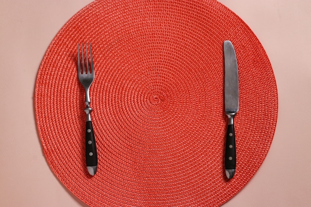 Ajuste de la tabla con una servilleta redonda de mimbre de color naranja, un tenedor y un cuchillo, para una persona, vista superior