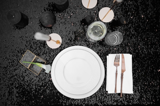 Ajuste de la tabla, vasos, velas y plato en negro, vista superior, nadie. Cubiertos de lujo, vajilla al aire libre, decoración elegante. Celebración romántica en la pradera de verano