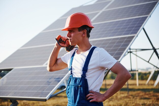 Akkuschrauber in der Hand. Männlicher Arbeiter in blauer Uniform im Freien mit Solarbatterien am sonnigen Tag.