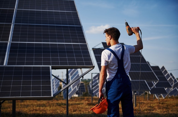 Akkuschrauber. Männlicher Arbeiter in blauer Uniform im Freien mit Solarbatterien am sonnigen Tag.