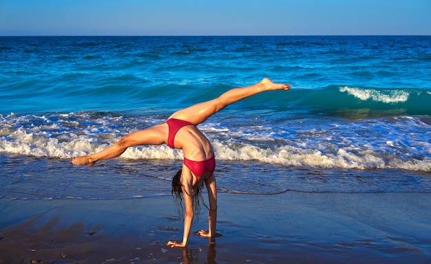 Akrobatisches Gymnastikbikinimädchen in einem Strand