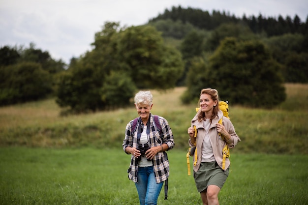 Aktive ältere Frau mit Fernglas, die mit ihrer erwachsenen Tochter im Freien in der Natur wandert