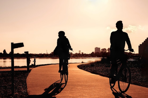 Aktive Freizeit in der Stadt bei Sonnenuntergang Silhouetten einer Frau und eines Mannes auf einem Fahrrad