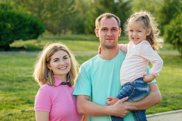 Aktive, glückliche Familie, die im Sommerpark mit einem Kinderwagen mit Tochter spazieren geht