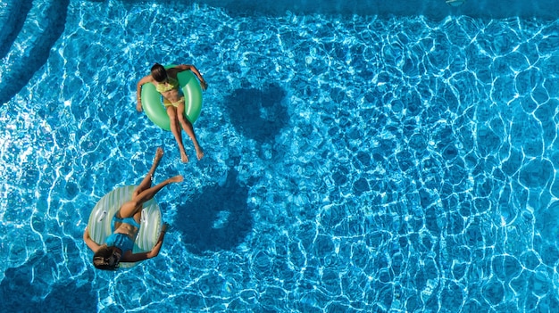 Aktive Kinder in der Luftaufnahme des Pools von oben, glückliche Kinder schwimmen auf aufblasbaren Ringkrapfen und haben Spaß im Wasser im Familienurlaub im Resort