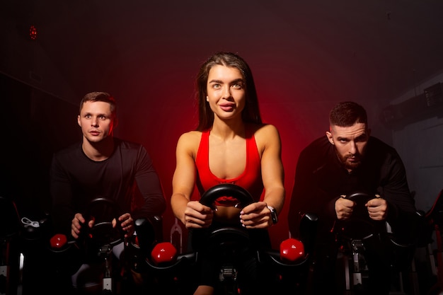 Aktive Menschen trainieren an Sportgeräten im Fitnessstudio, freuen sich zuversichtlich und tragen Trainingsanzüge in einem dunklen, rauchigen Raum