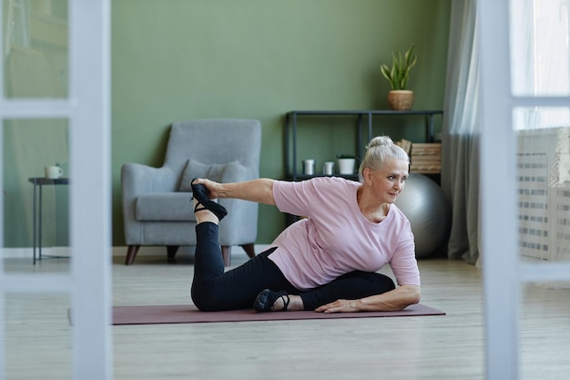 Aktive Seniorin, die Yoga-Asanas auf dem Boden praktiziert