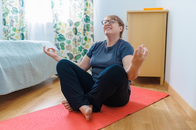 Aktive Seniorin, die zu Hause Bauchmuskelübungen auf Yogamatte macht und in die Kamera lächelt