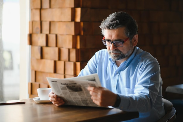 Aktiver älterer Mann liest Zeitung und trinkt Kaffee im Restaurant