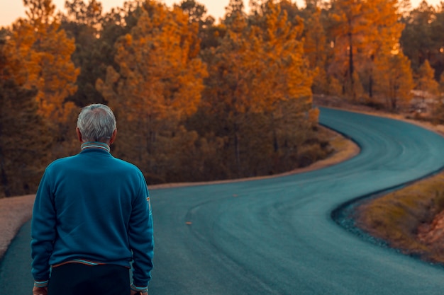 Aktiver älterer Mann steht allein auf einsamer Straße zwischen Bergen
