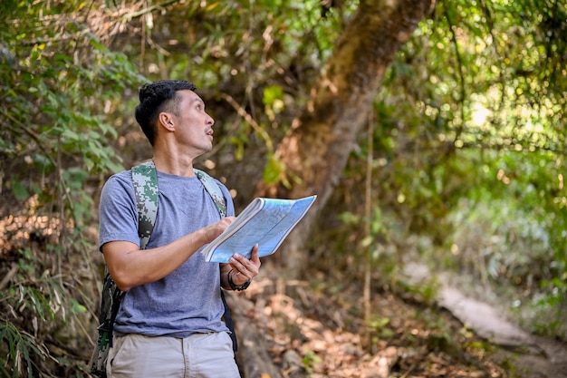 Aktiver asiatischer männlicher Trekker oder Reisender mit einem Rucksack, der die Trekkingroute auf der Karte betrachtet