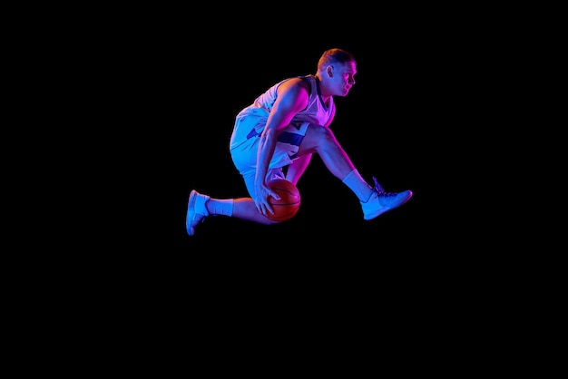 Aktiver athletischer männlicher Basketballspieler springt mit Basketballball einzeln auf dunklem Hintergrund