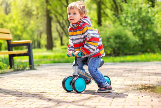 Aktiver blonder Junge fährt Balance- oder Laufrad im Freipark