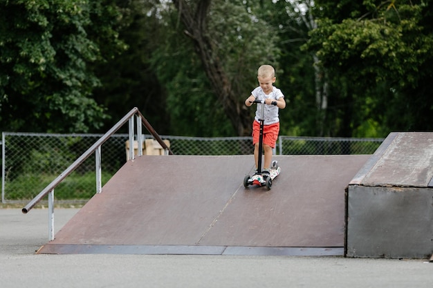 Aktiver Junge, der einen Roller im Sommer-Skatepark fährt