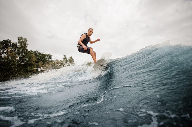 Aktiver Junge der Seitenansicht, der auf dem weißen Wakeboard reitet