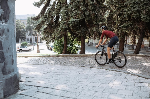 Aktiver kaukasischer Mann in Sportkleidung und Schutzhelm mit schwarzem Fahrrad auf der Stadtstraße Kaukasischer Radfahrer verbringt Freizeit für das Training im Freien