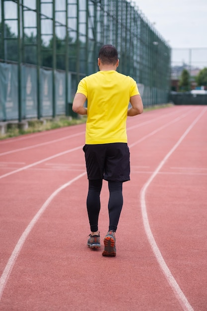 Aktiver Mann in Sportkleidung joggt entlang der Stadionstrecke gesunder und aktiver Lebensstil Rückwand