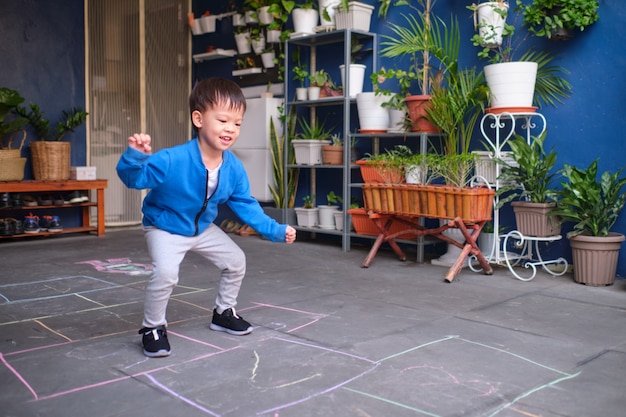 Aktiver netter lächelnder asiatischer Kleinkindjunge, der das Spaßspringen, Hopse zu Hause spielend hat