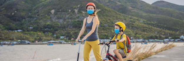 Aktiver Schuljunge und seine Mutter mit medizinischer Maske und Schutzhelm fahren Fahrrad mit Rucksack