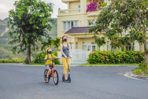 Aktiver Schuljunge und seine Mutter mit medizinischer Maske und Sicherheitshelm fahren mit Rucksack Fahrrad