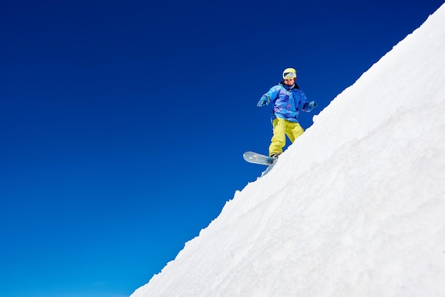 Aktiver Snowboarder, der an einem sonnigen Tag gegen den blauen Himmel auf einer weißen Piste im Hochgebirge reitet