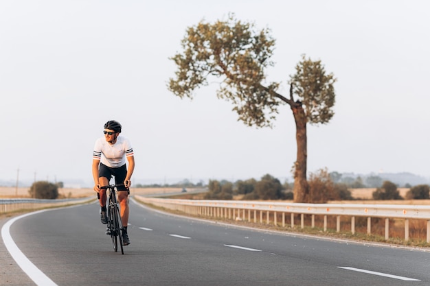 Aktiver Sportler im Schutzhelm und in der verspiegelten Brille, die Fahrrad während des sonnigen Tages im Freien reiten