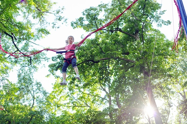 Aktives Erholungs- und Vergnügungspark-Kindermädchen im Freien, das Spaß beim Springen auf dem Trampolin mit elastischen Seilen hat