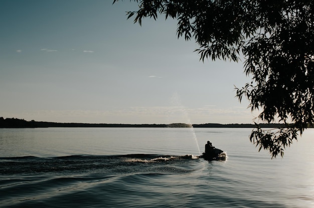 Aktives Freizeitsport-Hobby Silhouette von Menschen, die am Sommerabend Jetski auf dem Wasser des Sees fahren