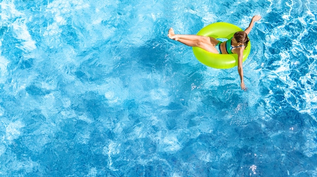 Aktives junges Mädchen in der Luftaufnahme des Schwimmbades von oben, Kind entspannt sich und schwimmt auf aufblasbarem Ringkrapfen und hat Spaß im Wasser im Familienurlaub, tropischer Ferienort