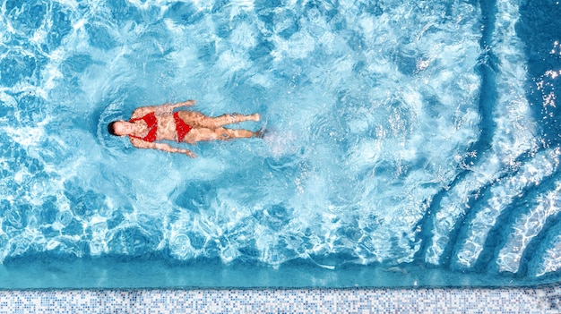 Aktives junges Mädchen in der Luftdrohnenansicht des Swimmingpools von oben Junge Frau schwimmt im blauen Wasser