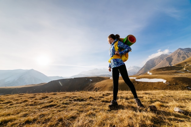 Aktives junges Mädchen in einer blauen Jacke reist mit Rucksack und Zelt durch den Kaukasus