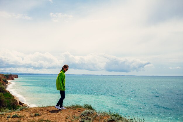 Aktives junges Mädchen in einer grünen Jacke reist, genießt das Meer und die Natur