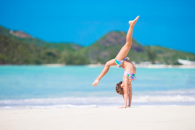 Aktives kleines Mädchen am Strand, der viel Spaß hat. Sportliches Kind, welches das Rad auf der Küste herstellt