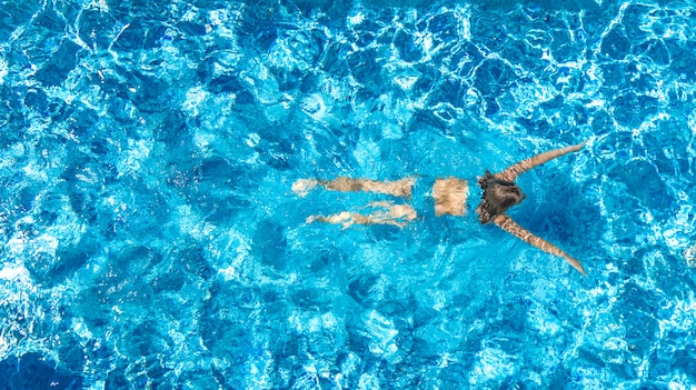 Aktives Mädchen in der Luftdrohnenansicht des Schwimmbades von oben, junge Frau schwimmt im blauen Wasser, tropischer Urlaub, Urlaub auf Resortkonzept