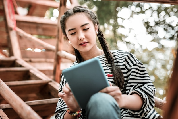 Aktives Messaging. Fröhliche asiatische Frau, die Lächeln auf ihrem Gesicht hält, während sie Bildschirm der Tablette betrachtet